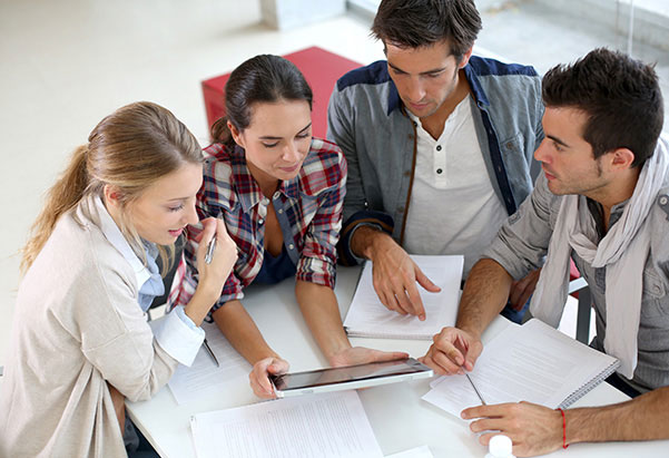 Four students sat at a desk all looking at a tablet, with papers on the desk